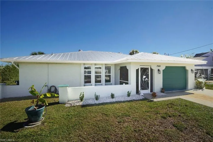 Ranch-style home featuring stucco siding, an attached garage, a front lawn, driveway, and a metal roof