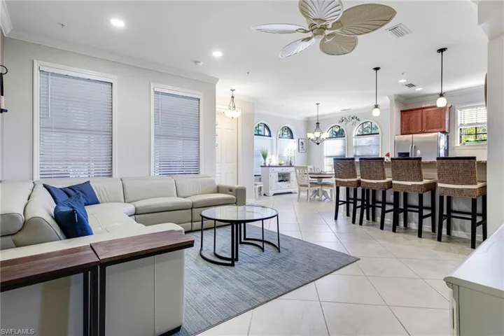 Living room featuring light tile patterned floors, crown molding, and ceiling fan with notable chandelier