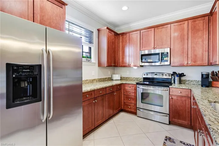 Kitchen featuring light stone counters, light tile patterned floors, crown molding, and stainless steel appliances
