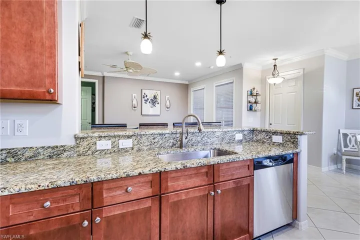 Kitchen featuring dishwasher, light stone countertops, sink, and decorative light fixtures