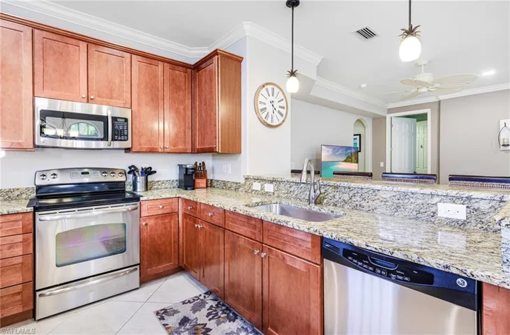 Kitchen featuring light stone counters, stainless steel appliances, decorative light fixtures, and sink