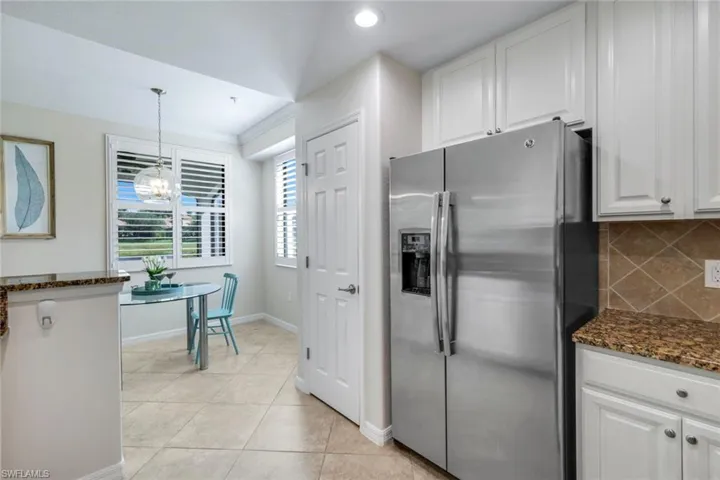 Kitchen featuring stainless steel fridge, white cabinetry, decorative backsplash, dark stone counters, and light tile patterned floors