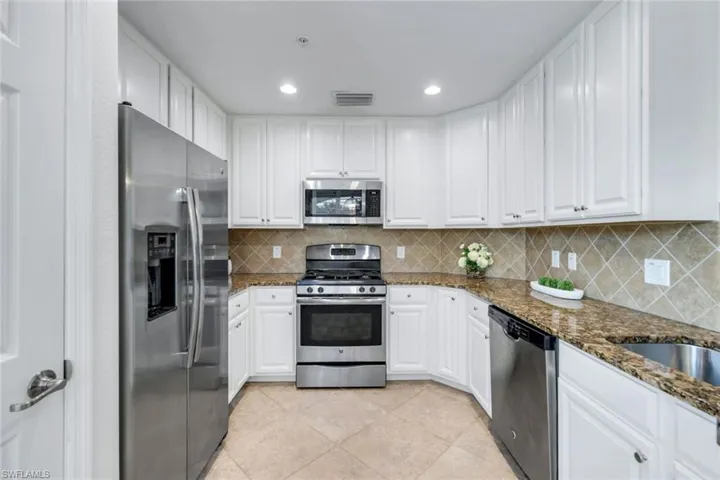 Kitchen with stainless steel appliances, white cabinets, dark stone counters, light tile patterned floors, and decorative backsplash