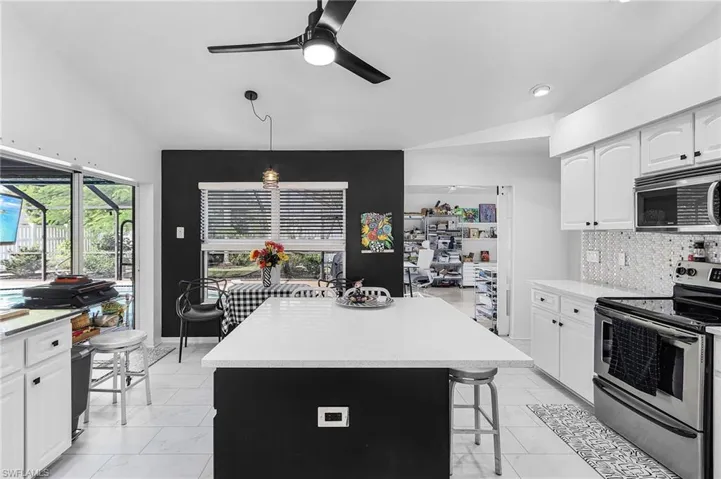 Kitchen featuring stainless steel appliances, a ceiling fan, white cabinets, decorative backsplash, and light stone countertops