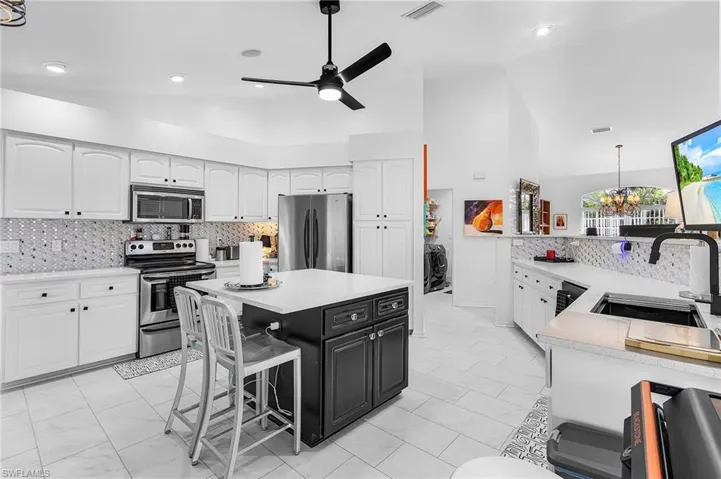 Kitchen with backsplash, lofted ceiling, dark cabinetry, stainless steel appliances, and a kitchen bar