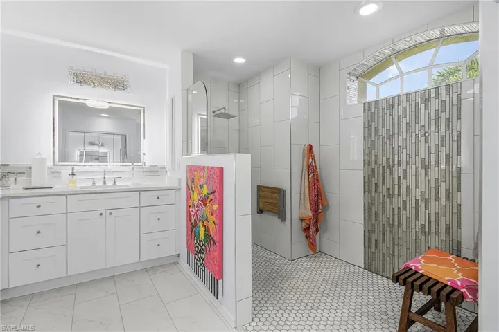 Bathroom featuring dual vanity, walk in family shower, and waterfall tile backsplash