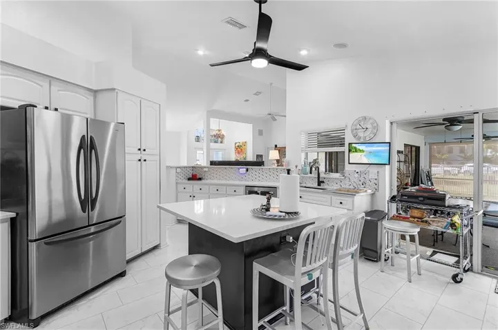 Kitchen featuring freestanding refrigerator, backsplash, and white cabinets, breakfast bar and ceiling fan