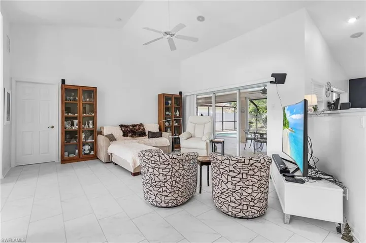 Living area with high vaulted ceiling and a ceiling fan and pocket sliders to the pool area, door to primary suite, open wall to the kitchen area and luxury vinyl flooring recently installed