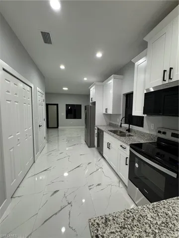 Kitchen with sink, white cabinets, stove, and light stone countertops