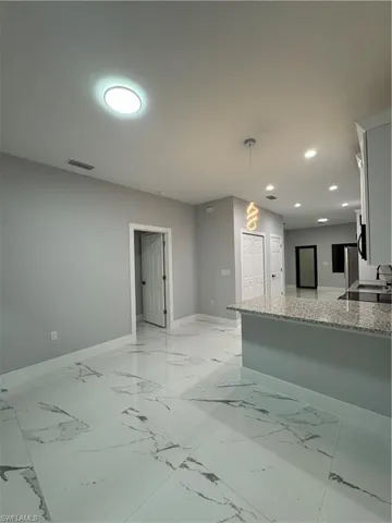 Kitchen with light stone counters, kitchen peninsula, decorative light fixtures, and white cabinetry