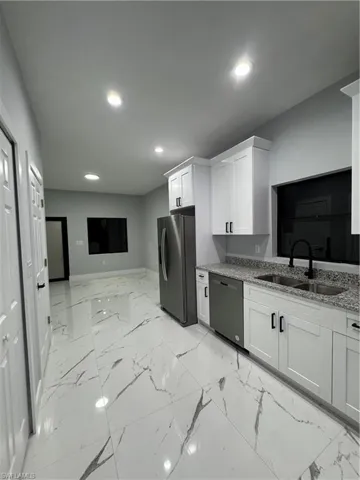 Kitchen with stainless steel refrigerator, light stone countertops, dishwashing machine, white cabinets, and sink