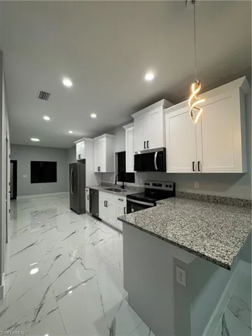 Kitchen with fridge, white cabinetry, stove, and kitchen peninsula