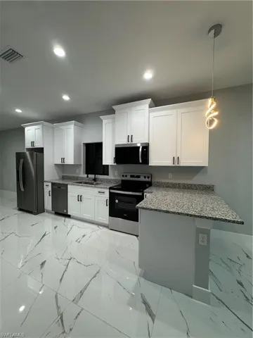 Kitchen featuring dishwasher, hanging light fixtures, refrigerator, white cabinetry, and stove