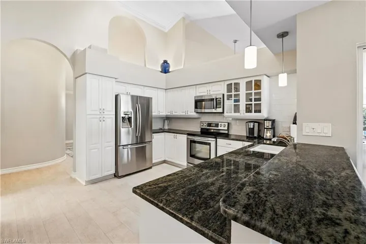Kitchen featuring glass insert cabinets, pendant lighting, stainless steel appliances, backsplash, and white cabinetry