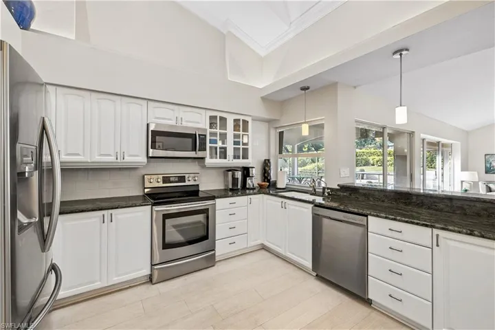 Kitchen featuring appliances with stainless steel finishes, white cabinetry, tasteful backsplash, decorative light fixtures, and crown molding
