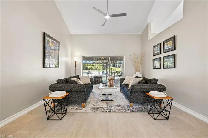 Living room featuring light wood-style flooring, crown molding, ceiling fan, and a towering ceiling
