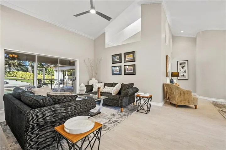 Living area with ornamental molding, a towering ceiling, light wood-type flooring, a ceiling fan, and a sunroom