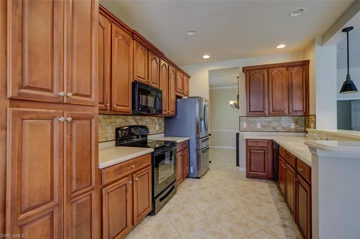 Kitchen featuring light tile patterned floors, black appliances, decorative backsplash, decorative light fixtures, and sink