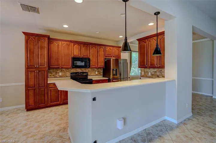 Kitchen with light tile patterned flooring, decorative backsplash, pendant lighting, and black appliances