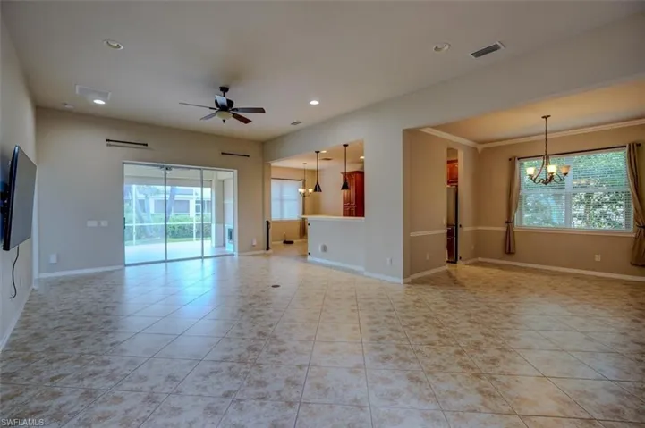 Unfurnished living room with light tile patterned flooring, a wealth of natural light, and ceiling fan with notable chandelier