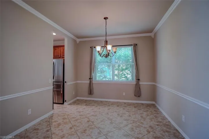 Empty room with crown molding, a notable chandelier, and light tile patterned floors