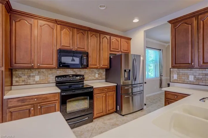 Kitchen featuring tasteful backsplash, black appliances, ornamental molding, and light tile patterned floors