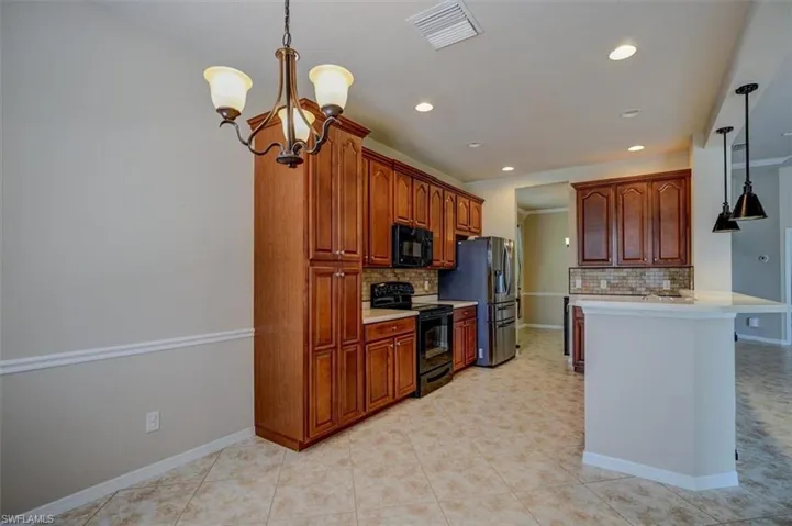 Kitchen with light tile patterned flooring, backsplash, black appliances, and hanging light fixtures