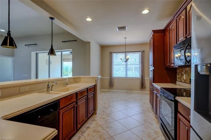 Kitchen with decorative light fixtures, black appliances, sink, and light tile patterned floors