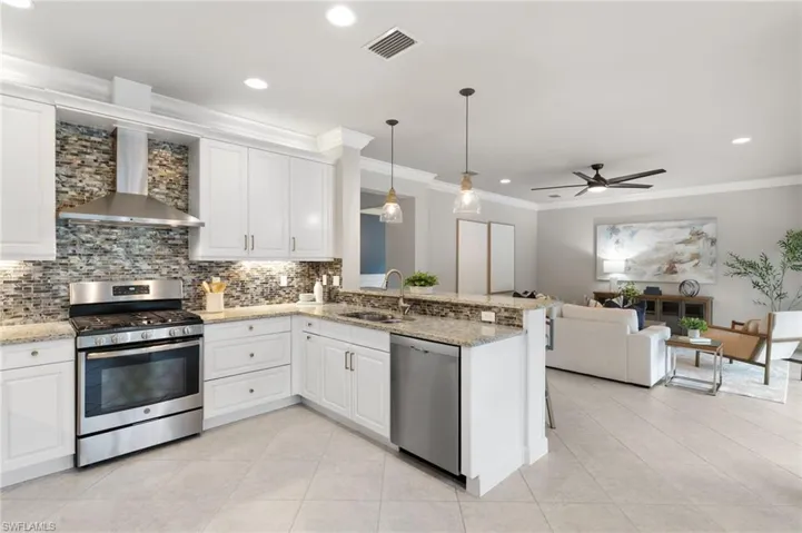 Kitchen with appliances with stainless steel finishes, decorative light fixtures, wall chimney exhaust hood, white cabinets, and crown molding