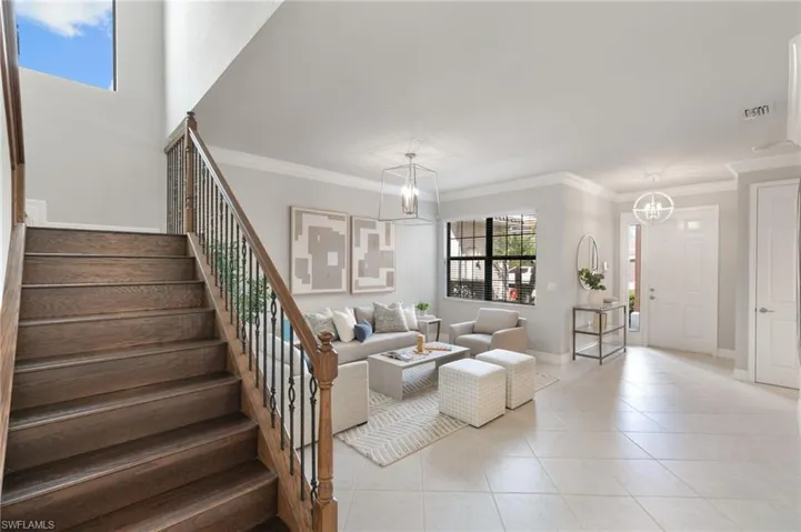 Tiled living area with crown molding, stairs, and a chandelier