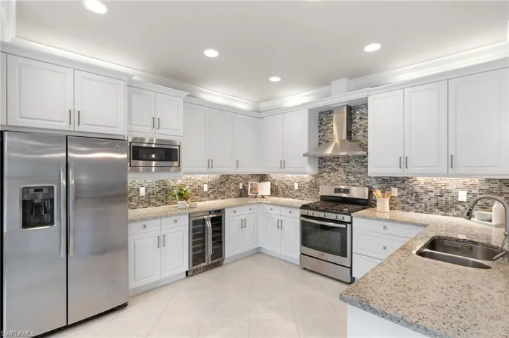 Kitchen featuring stainless steel appliances, white cabinets, light stone countertops, backsplash, and recessed lighting