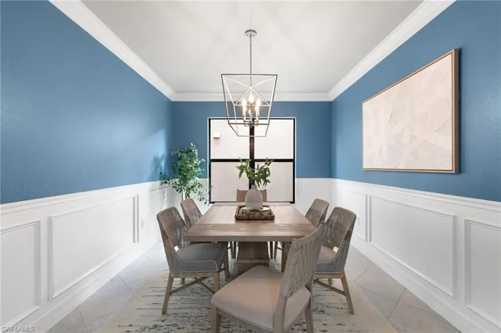 Tiled dining room featuring a decorative wall, wainscoting, ornamental molding, and a chandelier
