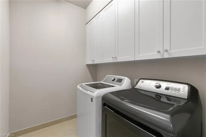 Laundry area with cabinet space, washing machine and clothes dryer, and light tile patterned flooring