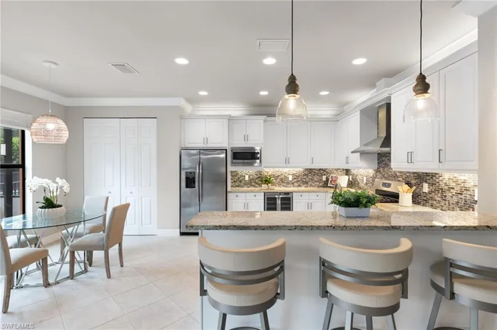 Kitchen with hanging light fixtures, tasteful backsplash, white cabinets, crown molding, and a peninsula