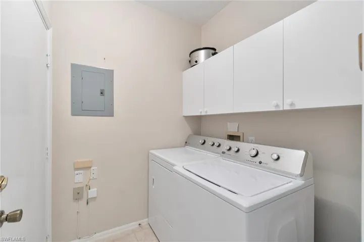 Laundry area with electric panel, cabinet space, separate washer and dryer, and light tile patterned floors