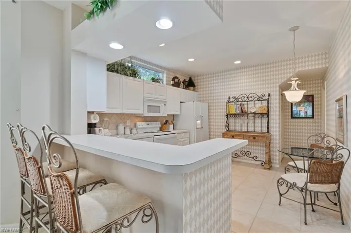Kitchen with recessed lighting, light countertops, white appliances, decorative light fixtures, and a peninsula