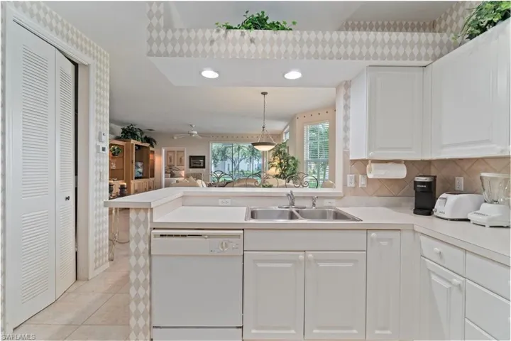 Kitchen featuring light countertops, white dishwasher, decorative backsplash, light tile patterned floors, and open floor plan