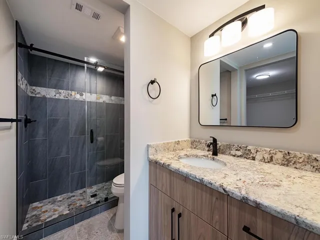 Bathroom featuring an enclosed shower, vanity, tile patterned floors, and toilet