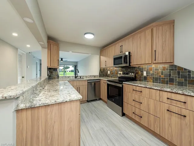 Kitchen with light stone counters, stainless steel appliances, a peninsula, decorative backsplash, and light wood-style flooring
