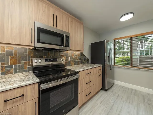 Kitchen featuring stainless steel appliances, light stone counters, tasteful backsplash, and modern cabinets