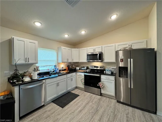 Kitchen with light wood finished floors, dark countertops, appliances with stainless steel finishes, vaulted ceiling, and a sink