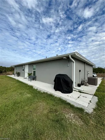 Rear view of house featuring a patio area, central AC, a lawn, and stucco siding