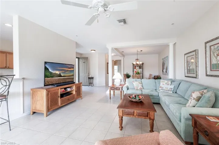 Living area with ornate columns, a ceiling fan, light tile patterned floors, a chandelier, and baseboards