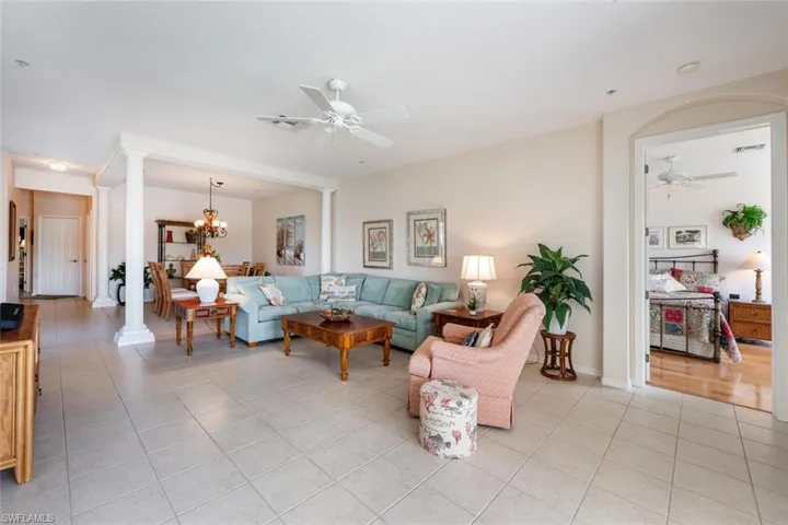 Living area with a ceiling fan, light tile patterned floors, ornate columns, a chandelier, and baseboards
