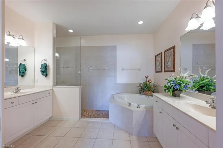 Master bathroom featuring tile patterned floors, a walk in shower, two vanities, a bath, and recessed lighting