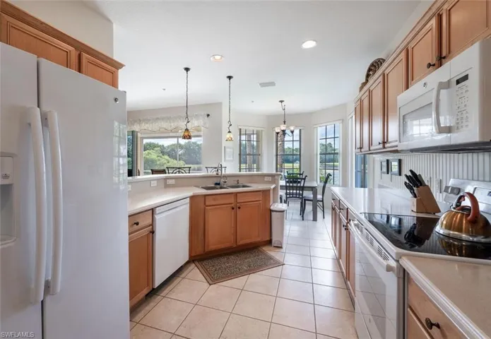 Kitchen featuring white appliances, a sink, light countertops, a chandelier, and recessed lighting