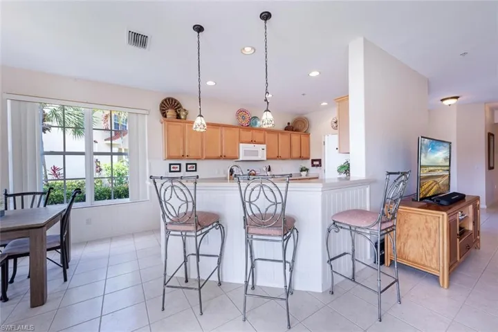 Kitchen with white microwave, a breakfast bar area, light tile patterned floors, light countertops, and recessed lighting