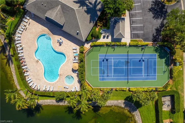 Aerial view showcasing the property's amenities, including a tennis court, a large swimming pool with an integrated spa, and a spacious pool deck with lounge seating