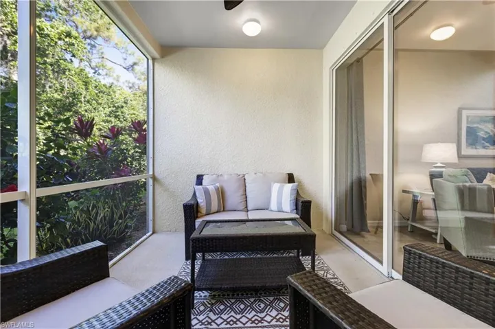 The screened patio features durable flooring, a patterned outdoor rug, and offers views of lush greenery