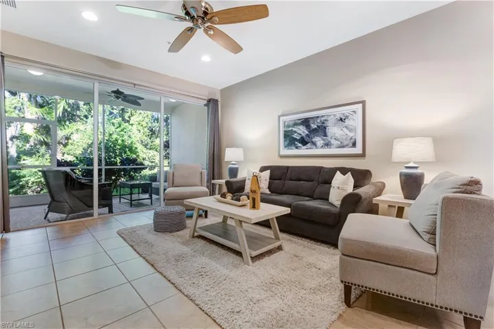 Living room with tiled flooring and a ceiling fan, opening to a screened patio with outdoor seating